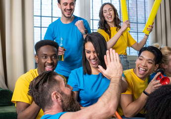 Group of diverse young friends celebrating with a high five during a team match at home. Joy, unity, and excitement captured in a moment of pure energy. Friendship and sports celebration concept.