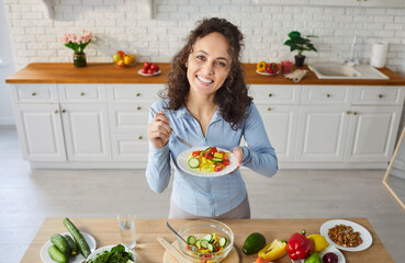 Portrait of a woman eating vegetable salad on kitchen at home, highlighting healthy food and...