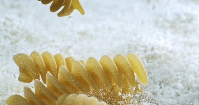 Macro of Fusilli Pasta Falling in Slow Motion on Floury Surface. Spiral Shape, Golden Texture, and Traditional Italian Cuisine Ingredients Captured in High-Detail for Culinary and Food Concepts