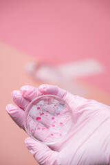 Breast cancer research concept, pink gloved hand holding a glass petri dish with pink bacteria.