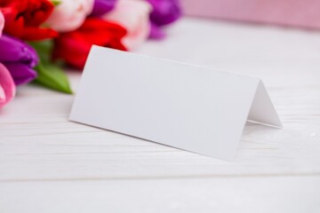 Blank tent card is standing on wooden tabletop beside blurred tulip bouquet, flat design copy space © vectorfusionart