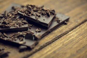 Dark chocolate bar pieces are stacking on rustic wooden surface in 3D render with fine shavings