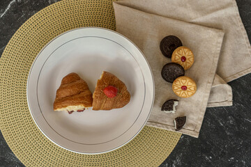 Flat lay of a breakfast plate with a jam-filled croissant. Chocolate and jam cookies are arranged...
