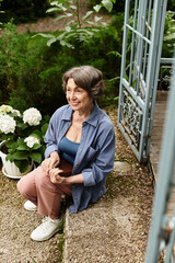 Joyful senior woman enjoying serenity in a vibrant garden during a sunny afternoon