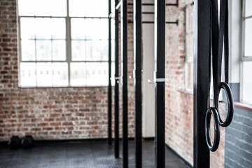 Flat design illustration showing gymnastic rings hanging from black beams in loft gym with window