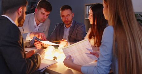 Colleagues or business people in team working together in office meeting, handling documents under light bulb glow, symbolizing ideas in a professional setting with focus and collaboration.