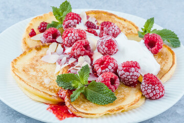 A plate of fluffy pancakes generously topped with fresh raspberries, whipped cream, and sprinkled with almond flakes, mint leaves on a gray background. Breakfast or sweet dessert concept. side view