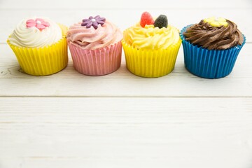 Four cupcakes are sitting on white tabletop in flat design with cream swirls and candy toppers
