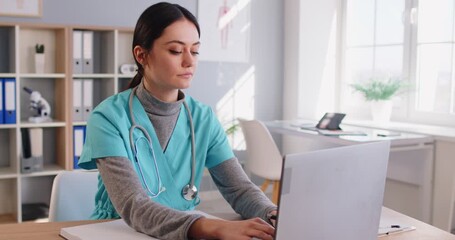 Female doctor working on computer. Young woman physician in green uniform scrubs typing on laptop, filling out EMRs, searching medical website database, preparing for consultation, or answering emails - Powered by Adobe