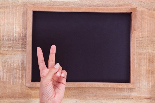 Flat design wooden-framed chalkboard with hand making V sign is being shown on wooden panel