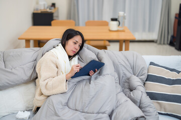 Woman feeling sick using tablet under blanket