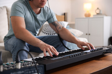 Man working with MIDI keyboard at table indoors, closeup