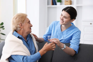 Obraz premium Nurse giving glass of water to senior woman indoors. Home health care service