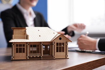Real estate agent working with client at desk in office, focus on house model