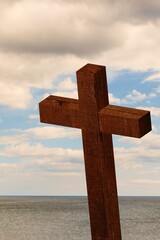 weathered wooden cross is standing before calm sea horizon under cloudy sky in flat design style