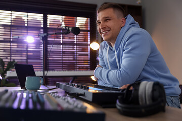Smiling man working with MIDI keyboard at table in home studio, low angle view