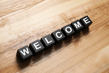 Word Welcome made of black cubes on wooden table, above view