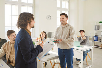 Young smiling cheerful student answering to a male teacher in the classroom during class lesson at...