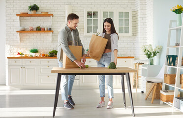 Couple unpacking shopping paper with food in modern kitchen, opening carton box, purchase from online store, happy with fast delivery service, buying groceries and household items, take away service