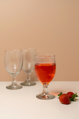 A glass of strawberry juice or rosé wine in focus, with two empty glasses in the background. A concept of serving drinks or tasting.