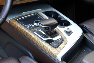 Close-up of automatic transmission selector in premium car brown leather interior. Luxury car gear shift lever in park mode. Modern rich brown leather interior with car stitching. Central car console.