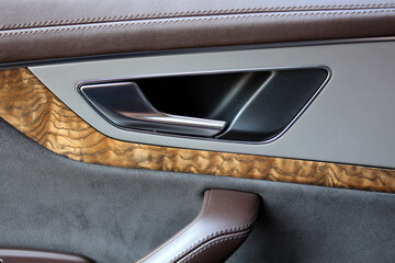 Close-up of a car door with brown leather upholstery and wood trim. The combination of materials...