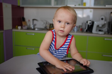 Baby is sitting at a table with a tablet in front of him