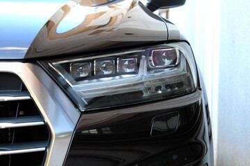 Close-up of a modern black cars right LED headlight and chrome grille with a glossy body surface...