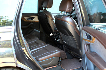 Rear view of a luxury car interior with brown leather seats, detailed stitching, and textured brown floor mats. Includes rear air vents, net storage, and premium trim elements.