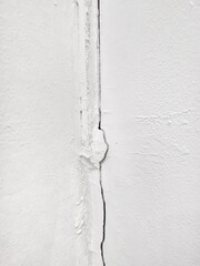 Straight crack on the old white painted concrete wall, up close. Damage to the wall is due to errors in building construction, weathering, earthquakes, heat waves, humidity, and weather changes.