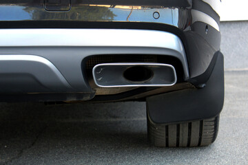 Obraz premium Close-up of a modern vehicle's rear bumper showcasing a rectangular chrome exhaust pipe. Glossy black and silver elements reflect surrounding objects, highlighting clean lines and technical precision
