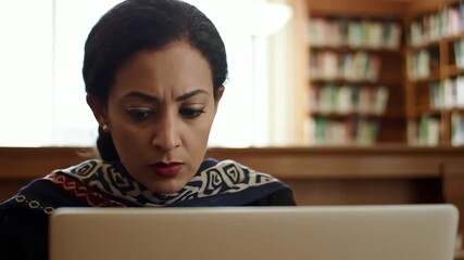 Focused mature female student with a concerned expression working on a laptop in a library