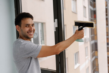Portrait of positive cleaning service employee spraying cleaning solution onto large window and...