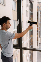 Vertical shot of young man spraying cleaning solution onto large window and wiping clean with...
