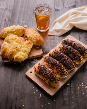 Assorted Indonesian sweet breads served on wooden cutting boards, including chocolate sprinkles bread (roti coklat meses) and cheese-topped bread (roti keju). Captured in warm natural lighting.
