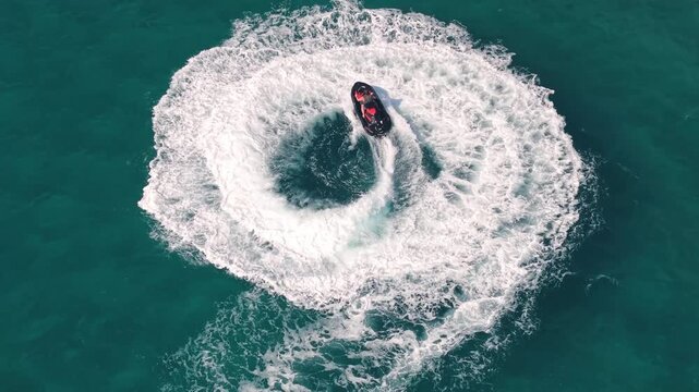 Homme en jet ski cr&eacute;ant des cercles de vagues blanches sur une mer bleue, film&eacute; en drone