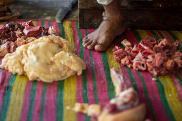 A butcher is cutting meat on a wooden stick with an iron tool.
