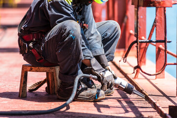 A crew member working on the deck of a merchant ship, using a pneumatic tool to remove rust.
