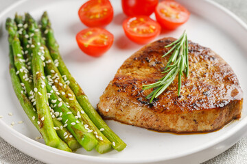 Close up, macro of tasty grilled beef steak served with green asparagus and cherry tomatoes on white plate, with cutlery. Perfect for food menu, diet, or culinary design concepts.