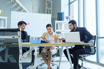 Asian business team meeting in modern office, collaborating over documents and laptop to discuss strategy, goals, and project development in professional setting.