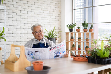 An old man is reading a newspaper in a room with potted plants.