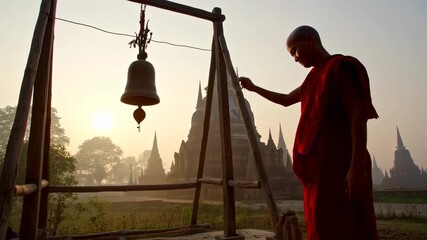 Buddhist monk ringing a bell at sunrise, ancient temples in the background