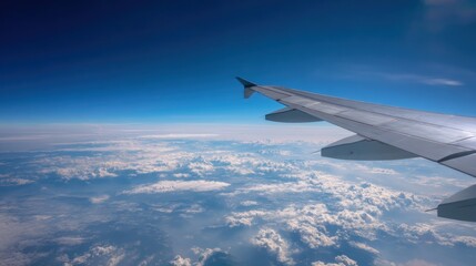 Obraz premium Airplane wing and vast blue sky seen from window seat, bright daylight and minimal clouds