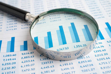 Magnifying glass on spreadsheet and graph paper.