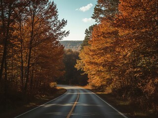 Autumn road winds through a forest with orange foliage under a blue sky, a seasonal scenic drive.