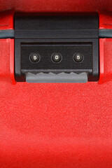 A close-up vertical shot focuses on the numerical combination lock mechanism of a red suitcase,...