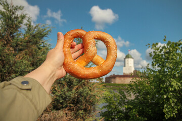 Traditional pretzel pastry in hand against backdrop of Olaf's Tower in city Vyborg, Russia on sunny day