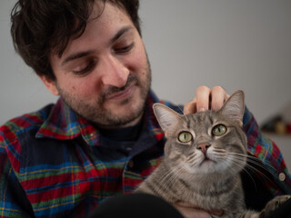 Chat gris caress&eacute; sur la t&ecirc;te par son ma&icirc;tre souriant en chemise &agrave; carreaux
