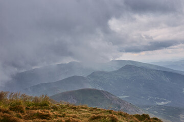 Cloudy mountain landscape near valley during afternoon with overcast sky and distant peaks visible...