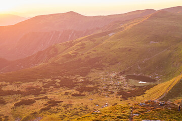 Majestic mountain landscape at sunset with serene Nesamovyte lake reflecting golden hues in the...